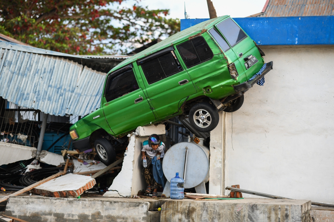 Sobrevivente perto de um carro preso em um prédio em Palu (Foto: AFP PHOTO / Jewel SAMAD; Ola Gondronk; Adek BERRY; Mohd RASFAN)