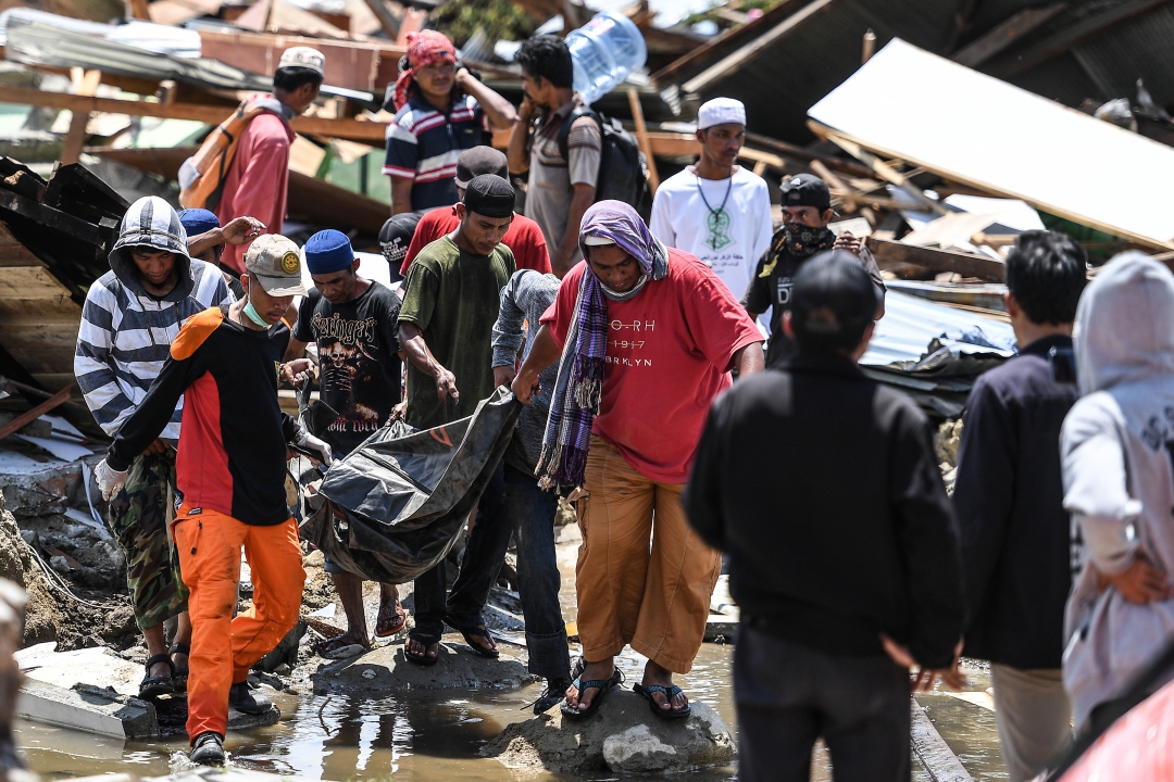 Moradores e equipes de resgate carregam o corpo de uma vítima do terremoto em aldeia de Palu (Foto: AFP PHOTO / Jewel SAMAD; Ola Gondronk; Adek BERRY; Mohd RASFAN)