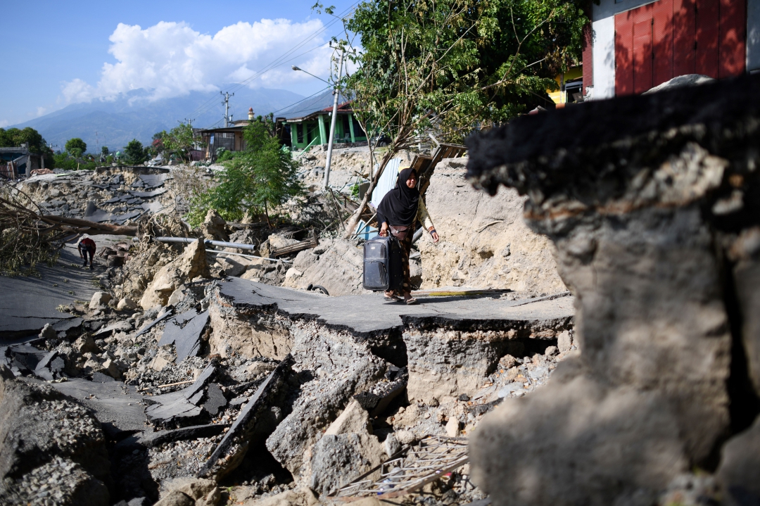 Mulher com uma mala caminha ao longo de uma estrada destruída em Palu
(Foto: AFP PHOTO / Jewel SAMAD; Ola Gondronk; Adek BERRY; Mohd RASFAN)