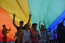 Participantes da Parada Gay embaixo de um bandeir&atilde;o com as cores do arco-&iacute;ris