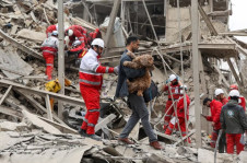 Um homem carrega um cachorro enquanto o pessoal de emerg&ecirc;ncia trabalha no local de um ataque a um pr&eacute;dio residencial em Teer&atilde;, em meio ao conflito com EUA-Israel